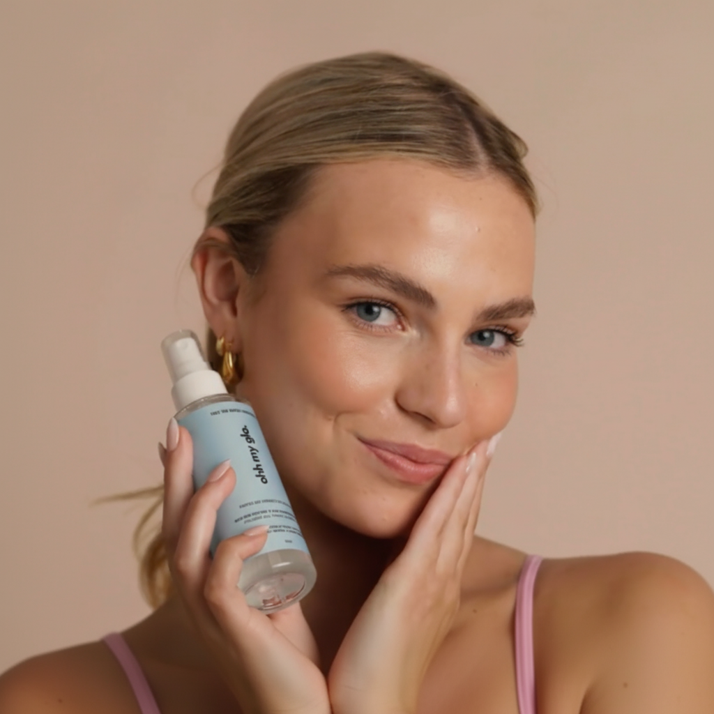 Model holding face tan water to her ace with a golden glow